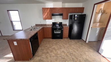 Kitchen with black appliances, dark countertops, a peninsula, brown cabinetry, and under cabinet range hood