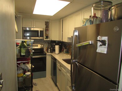 Kitchen with stainless steel appliances, light tile patterned flooring, backsplash, and white cabinetry