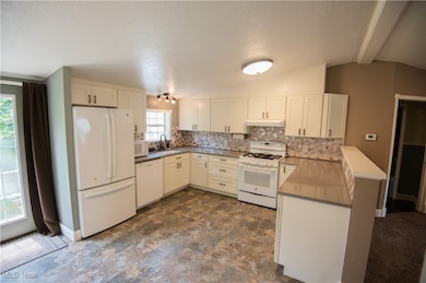 Kitchen featuring white appliances, a peninsula, lofted ceiling, decorative backsplash, and a textured ceiling