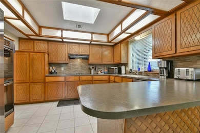 Kitchen with a peninsula, tasteful backsplash, brown cabinetry, and a textured ceiling