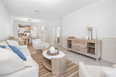 Living room with light tile patterned floors, a wainscoted wall, a decorative wall, and a chandelier
