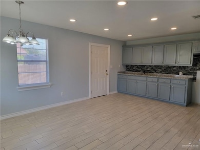 Kitchen featuring gray cabinets, decorative backsplash, light wood-type flooring, baseboards, and a chandelier