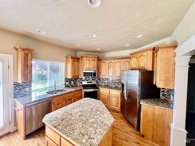 Kitchen featuring backsplash, stainless steel appliances, light stone counters, light wood finished floors, and a center island