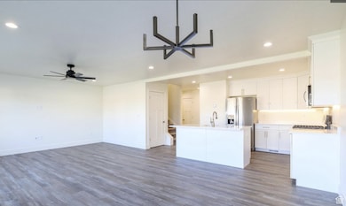 Kitchen with open floor plan, wood finished floors, recessed lighting, an island with sink, and white cabinetry