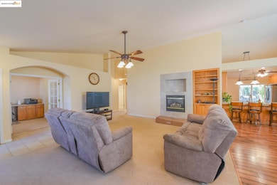 Living area featuring a ceiling fan, a tiled fireplace, built in features, arched walkways, and light colored carpet