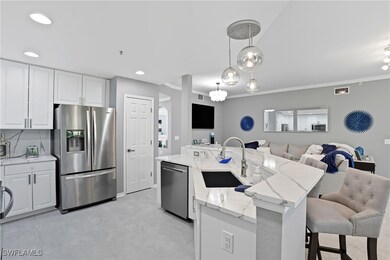 Kitchen featuring appliances with stainless steel finishes, an island with sink, white cabinetry, pendant lighting, and ornamental molding