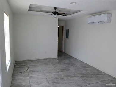 Empty room featuring an AC wall unit, a tray ceiling, ceiling fan, baseboards, and light marble finish floors