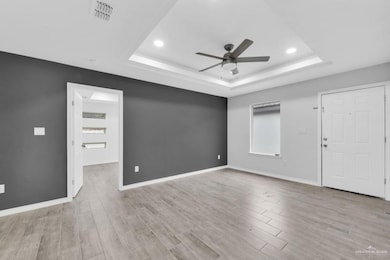 Spare room featuring light wood-type flooring, a ceiling fan, a raised ceiling, and recessed lighting
