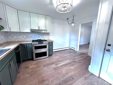 Kitchen with white cabinetry, tasteful backsplash, stainless steel appliances, decorative light fixtures, and light wood finished floors