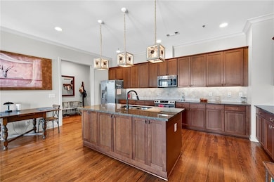 Kitchen featuring stainless steel appliances, dark wood finished floors, a center island with sink, dark stone counters, and tasteful backsplash