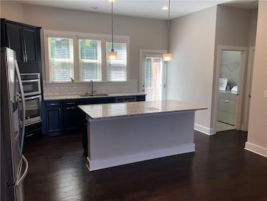 Kitchen featuring appliances with stainless steel finishes, separate washer and dryer, dark wood-type flooring, decorative backsplash, and light stone counters