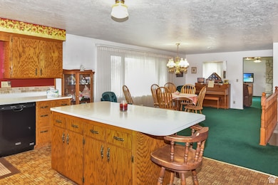 Kitchen featuring a textured ceiling, dishwasher, light countertops, brown cabinetry, and a kitchen breakfast bar
