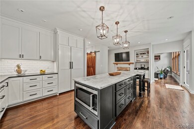 Kitchen with pendant lighting, dark wood-type flooring, a barn door, stainless steel microwave, and a kitchen island