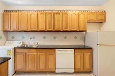 Kitchen with white appliances, washer / clothes dryer, decorative backsplash, dark stone counters, and light tile patterned floors