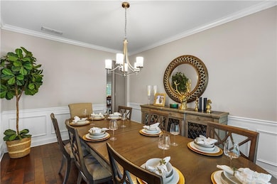 Dining space featuring a decorative wall, a wainscoted wall, crown molding, dark wood-style flooring, and a chandelier