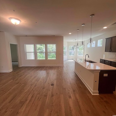 Kitchen with pendant lighting, open floor plan, a center island with sink, light stone countertops, and dark wood-type flooring