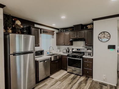STAGED Kitchen featuring stainless steel appliances, light countertops, dark brown cabinetry, crown molding, and recessed lighting
