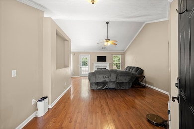 Living area featuring a ceiling fan, crown molding, wood finished floors, baseboards, and a fireplace