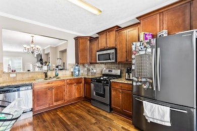 Kitchen featuring stainless steel appliances, a chandelier, brown cabinets, ornamental molding, and tasteful backsplash