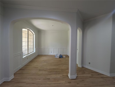 Spare room with arched walkways, wood finished floors, crown molding, and a wainscoted wall