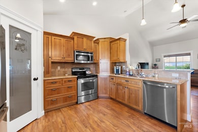 Kitchen with stainless steel appliances, a peninsula, decorative backsplash, light wood-type flooring, and high vaulted ceiling