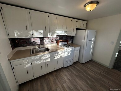 Kitchen featuring white cabinetry, white appliances, tasteful backsplash, dark wood finished floors, and light countertops