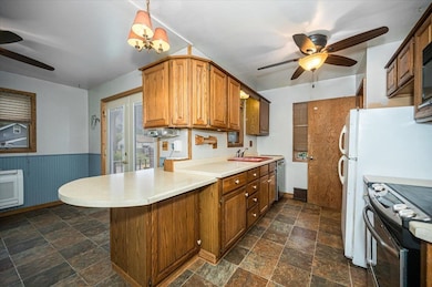 Kitchen with a ceiling fan, a peninsula, light countertops, dark stone finish flooring, and a wainscoted wall