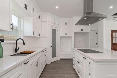 Kitchen with island exhaust hood, a sink, black electric stovetop, white cabinetry, and decorative backsplash