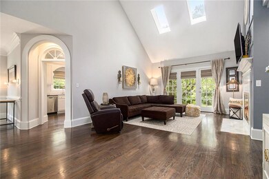 Living area with high vaulted ceiling, wood finished floors, a skylight, and arched walkways
