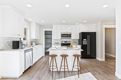 Kitchen featuring stainless steel appliances, decorative backsplash, a kitchen breakfast bar, white cabinetry, and recessed lighting