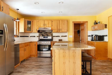 Kitchen with appliances with stainless steel finishes, tasteful backsplash, a center island, light wood finished floors, and a breakfast bar area