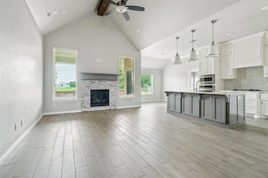 Unfurnished living room with ceiling fan, beamed ceiling, high vaulted ceiling, light wood-style floors, and a stone fireplace