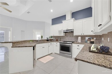 Kitchen with stainless steel appliances, range hood, a peninsula, decorative backsplash, and ceiling fan