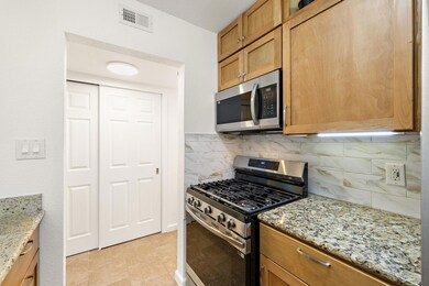 Kitchen featuring appliances with stainless steel finishes, tasteful backsplash, light stone counters, and light tile patterned flooring
