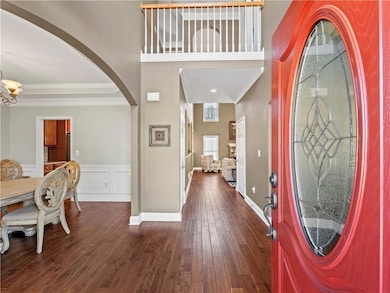 Foyer entrance with dark wood finished floors, crown molding, arched walkways, wainscoting, and a chandelier