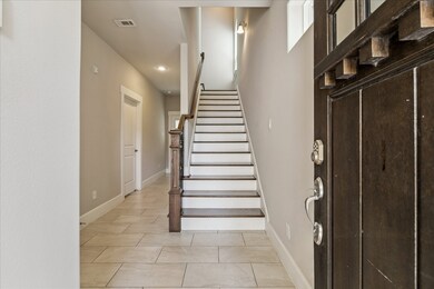 A welcoming foyer leads to the main living areas, with neutral tile flooring and a wood-accent staircase that adds warmth and character. Natural light filters from the upper windows, creating an airy first impression.