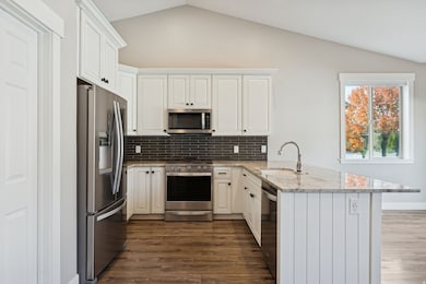 Kitchen with light stone counters, appliances with stainless steel finishes, vaulted ceiling, decorative backsplash, and a peninsula