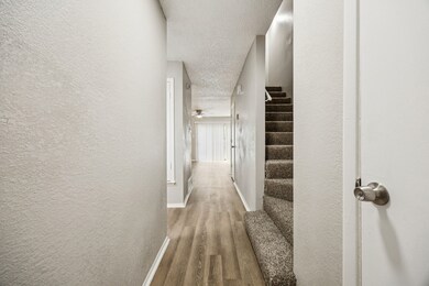 Hallway with a textured wall, light wood finished floors, stairs, and a textured ceiling