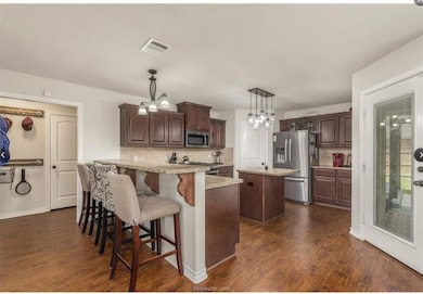 Kitchen featuring a peninsula, hanging light fixtures, a kitchen bar, appliances with stainless steel finishes, and dark wood-type flooring