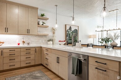 Kitchen featuring light brown cabinetry, open shelves, pendant lighting, light wood-style flooring, and a textured ceiling