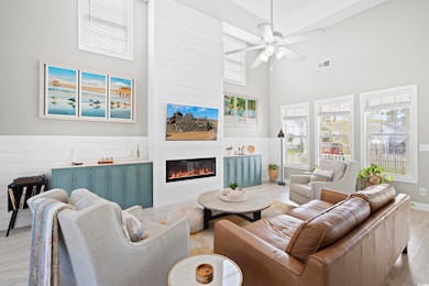 Living area featuring a large fireplace, a towering ceiling, visible vents, a ceiling fan, and wood finished floors