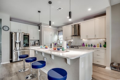 Kitchen with appliances with stainless steel finishes, wall chimney exhaust hood, backsplash, light countertops, and a center island with sink