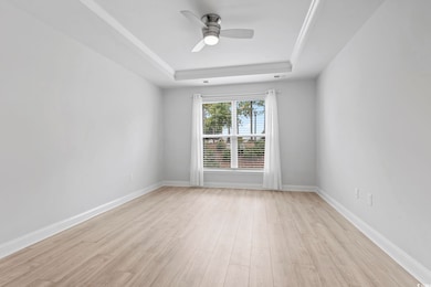 Bedroom featuring a raised ceiling, light wood finished floors, and ceiling fan