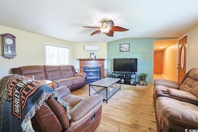 Living area featuring a glass covered fireplace, light wood finished floors, vaulted ceiling, a wall mounted air conditioner, and a ceiling fan