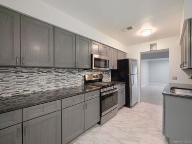 Kitchen featuring stainless steel appliances, gray cabinetry, decorative backsplash, and light marble finish floors