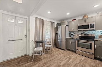 Kitchen with stainless steel appliances, gray cabinetry, decorative backsplash, light wood finished floors, and light stone countertops