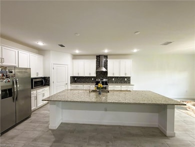 Kitchen featuring stainless steel appliances, decorative backsplash, wall chimney range hood, a large island with sink, and white cabinets
