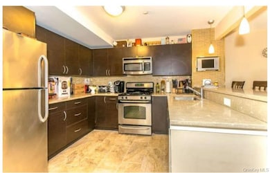 Kitchen featuring appliances with stainless steel finishes, dark brown cabinetry, decorative light fixtures, tasteful backsplash, and light stone counters