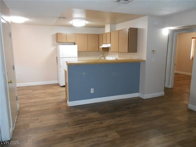 Kitchen featuring freestanding refrigerator, a peninsula, dark wood-style flooring, a textured ceiling, and under cabinet range hood