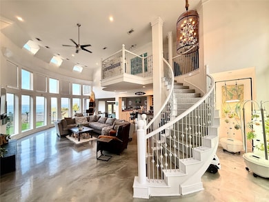 Living room featuring concrete flooring, a towering ceiling, a ceiling fan, recessed lighting, and a chandelier